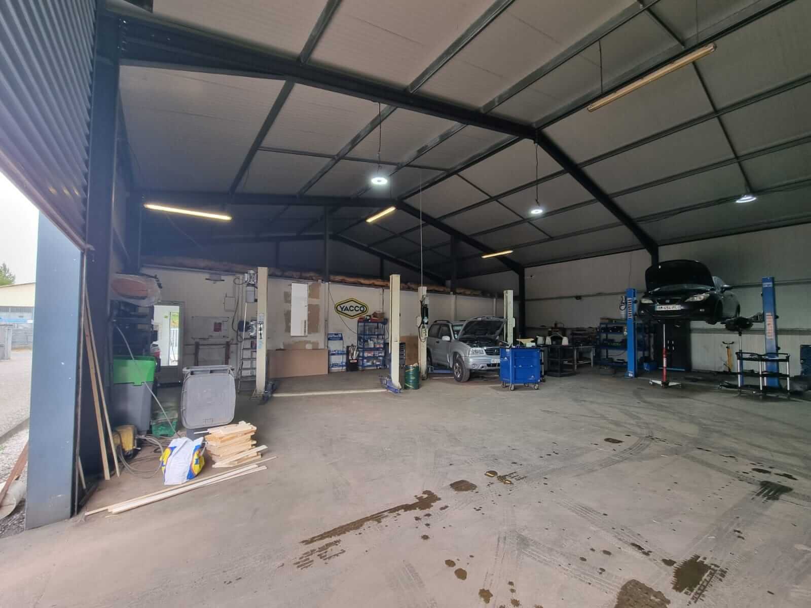 Intérieur du garage avec plusieurs voitures sur ponts élévateurs et matériel d’atelier.